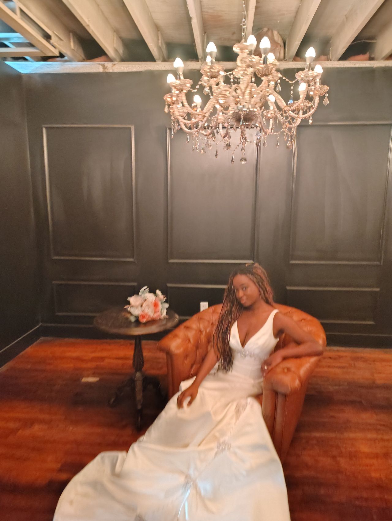 A bride seated on a tan leather sofa in the Speakeasy, her gown and train spread across the historic hardwood floor