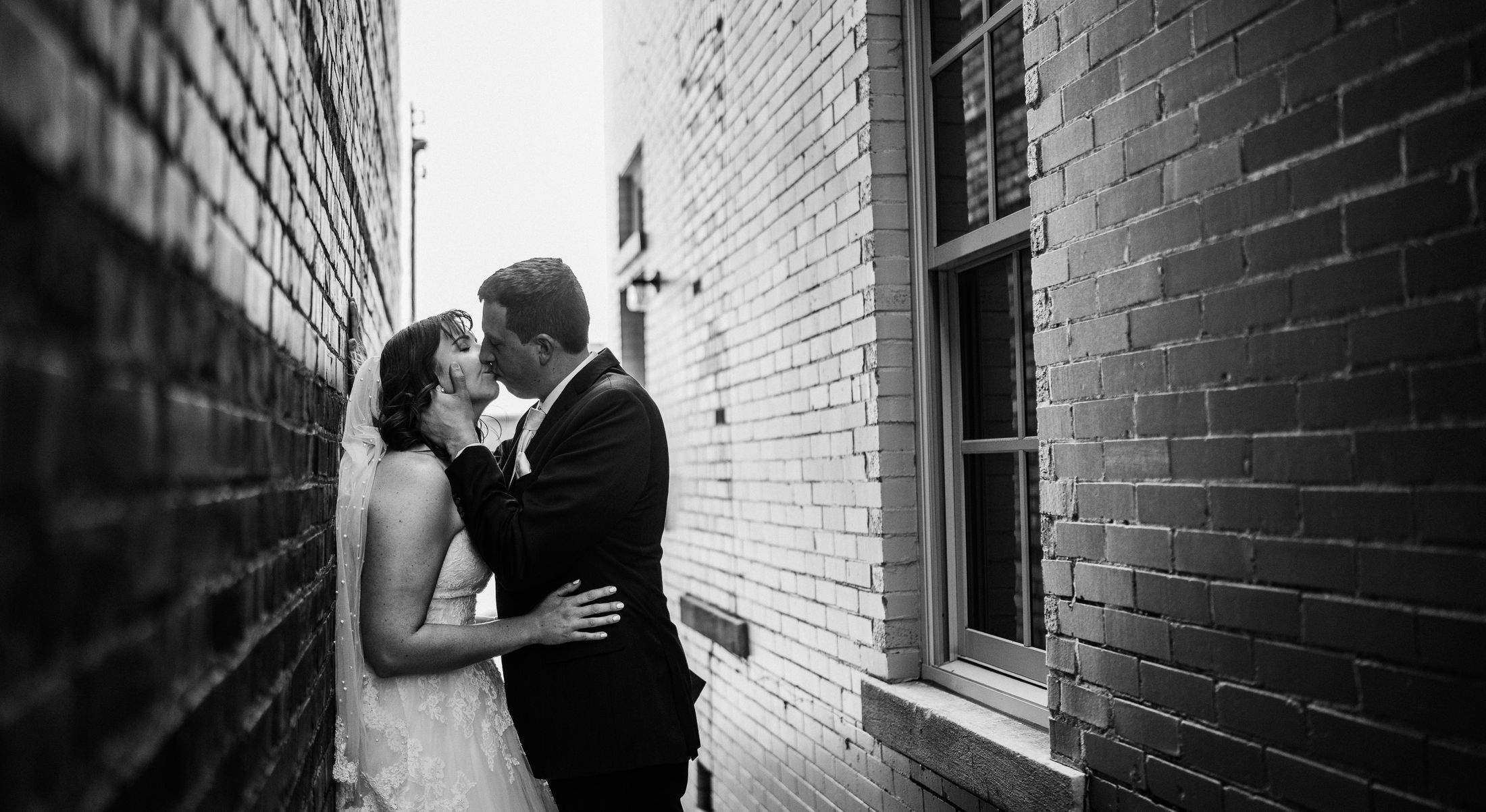 A bride and groom in a brick alley beside the building, photographed in black and white