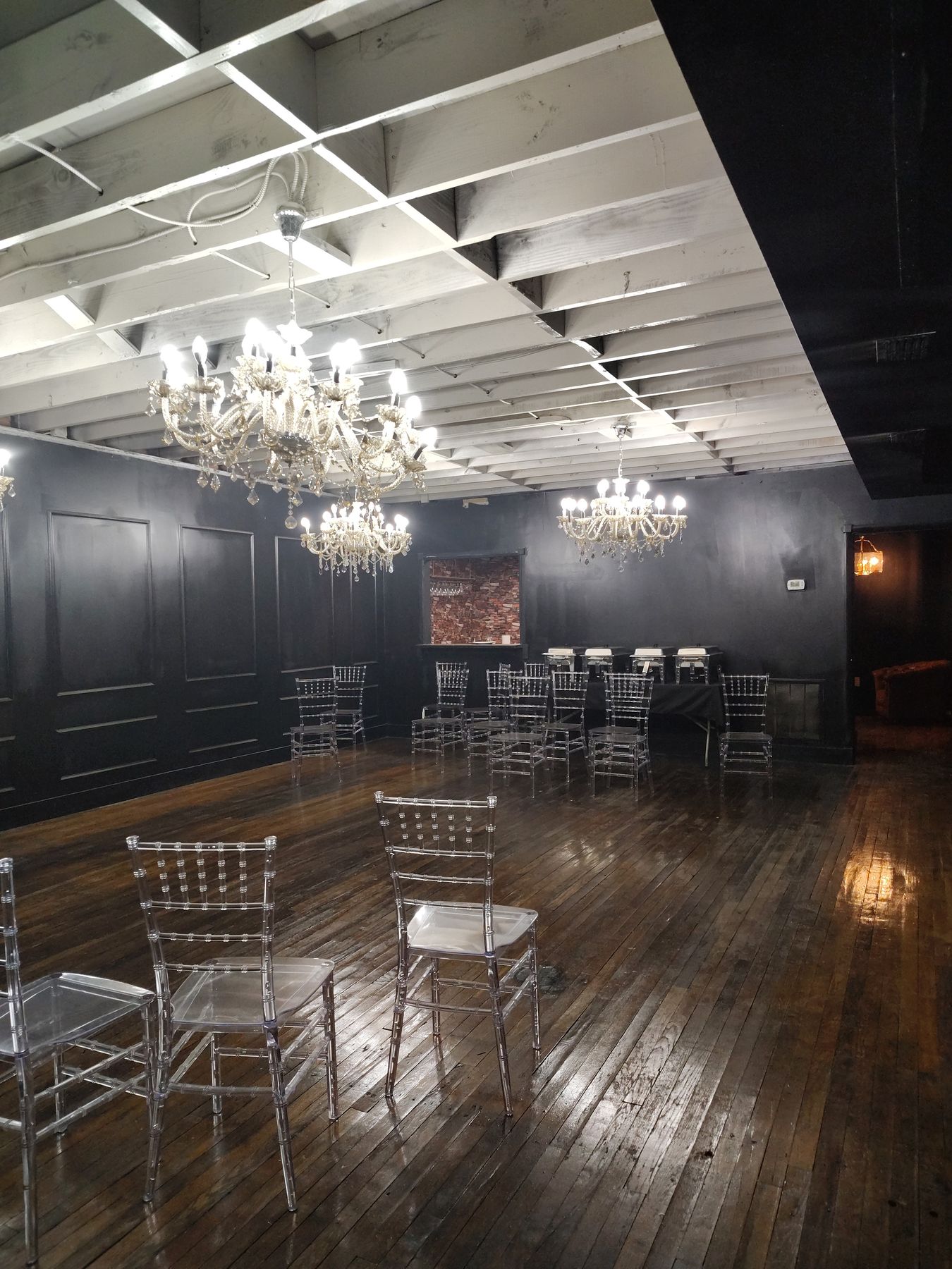 The empty Speakeasy in daylight, with black paneled walls, a brass chandelier and sunlight falling across the 1890s hardwood